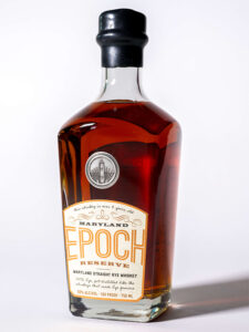 A bottle of Maryland Epoch Reserve straight rye whiskey by Baltimore Spirits Company, featuring amber liquid, a gold and white label, and a black cap, shown against a plain white background.