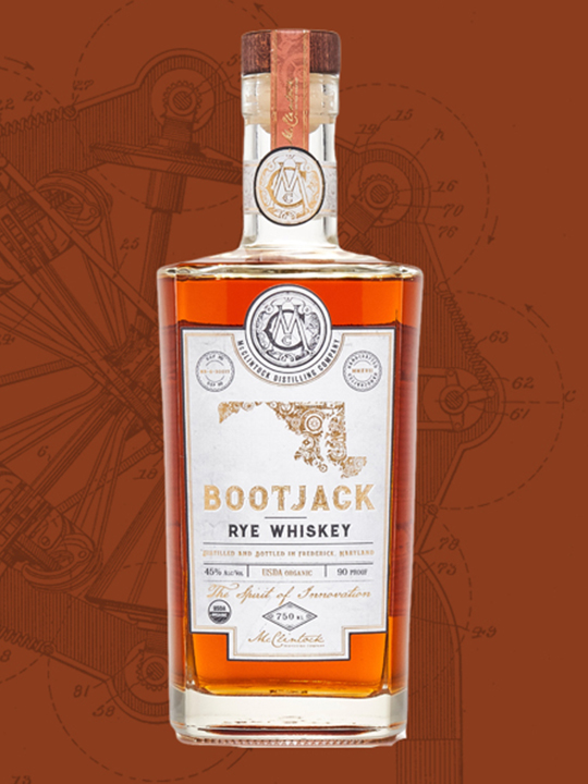 A bottle of Bootjack Rye Whiskey from Baltimore Spirits Company, with a white and gold label, stands against a brown background adorned with faint mechanical drawings.