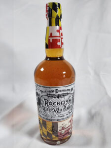 A bottle of Rockfish Rye Whiskey from Baltimore Spirits Company, featuring a detailed black and white label with a Maryland flag design on the neck and bottom. The bottle is displayed against a plain white background.